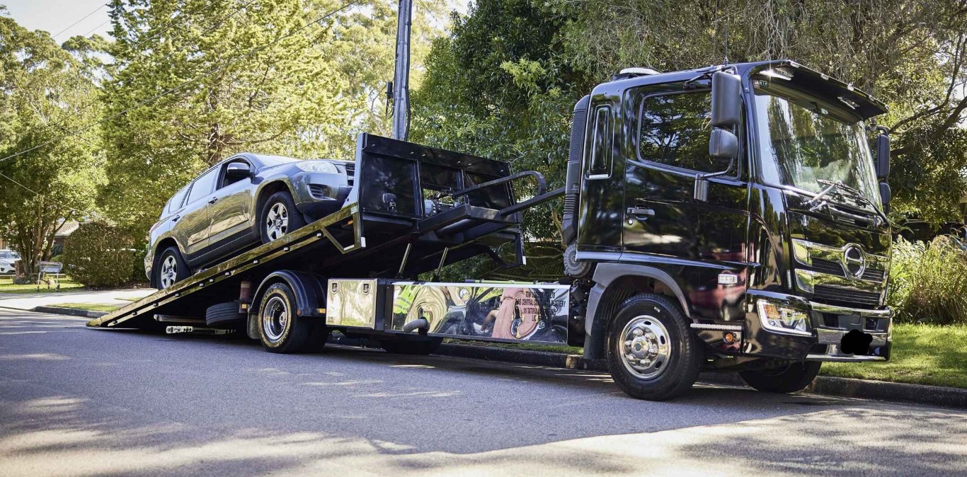 Black flatbed tow truck loading a dark SUV in a suburban neighborhood