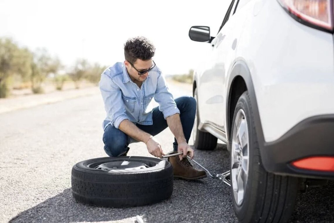 Man changing a flat tire on a white vehicle at the roadside