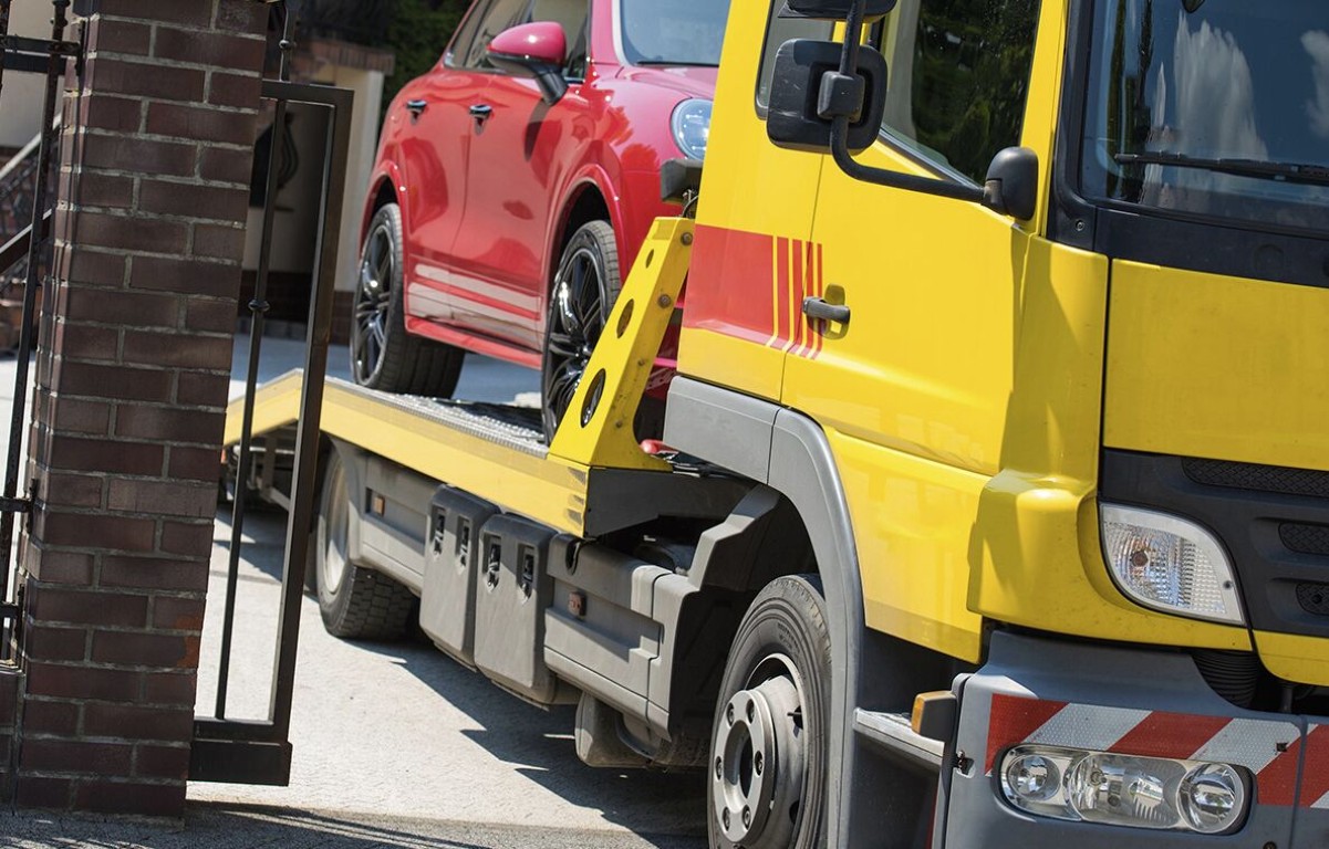 Yellow flatbed tow truck carrying a red car through a residential area near North Babylon, NY