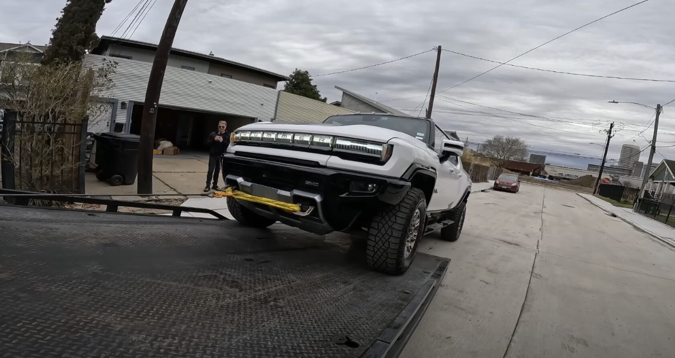 Tow service technician loading a large vehicle onto a flatbed for battery replacement assistance