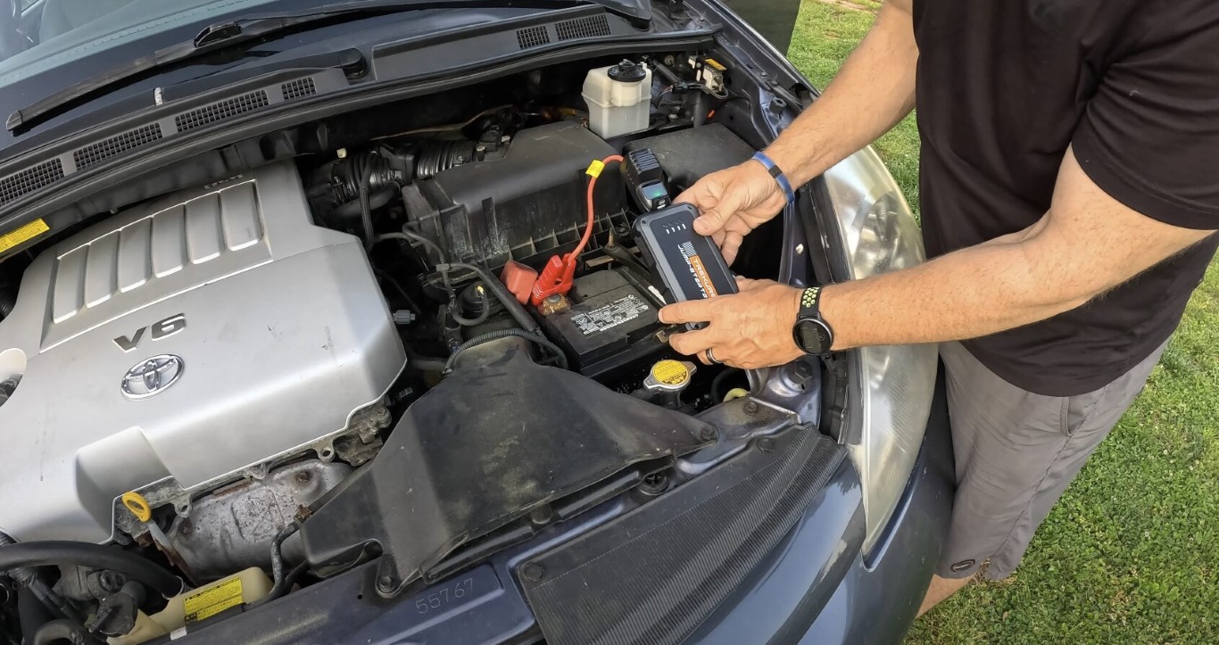 Technician performing a jump start on a dead car battery under the hood in Deer Park, NY