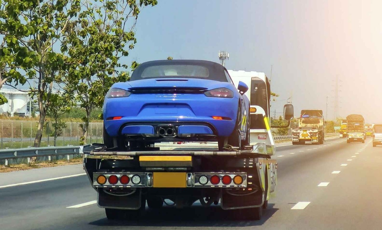 Flatbed tow truck transporting a blue sports car on a highway for long distance towing