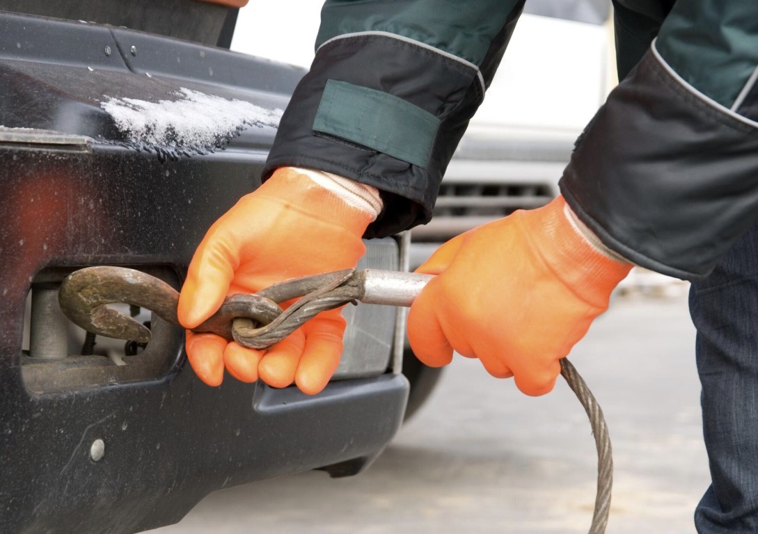 Tow truck technician attaching a winch hook to a vehicle bumper for winch out recovery